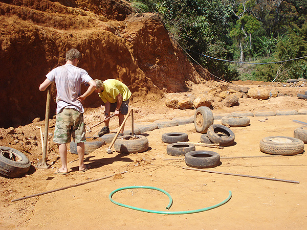 Two builders ramming the first tyres in January 2009 — red earth, jungle hillside behind them
